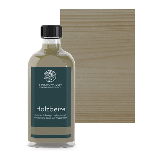 Holzbeize Kieselgrau in der Glasflasche mit gebeiztem Holz im Hintergrund.