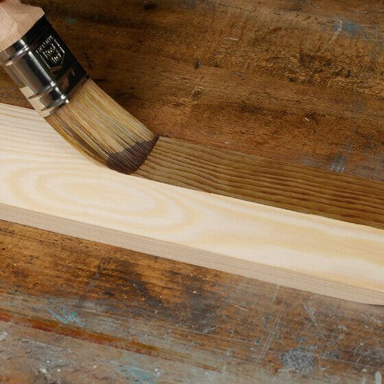 Beize Nussbaum dunkel wird mit Pinsel auf einem kleinen Brett aufgestrichen.