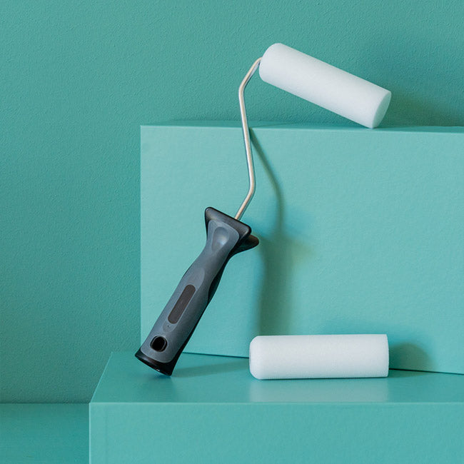 Kurzer Aufsteckbügel mit zwei kleinen Schaumstoffwalzen auf grünem Podest vor grüner Wand