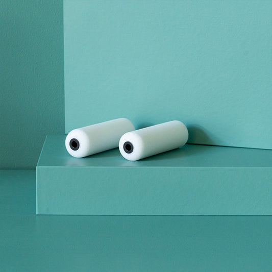 Zwei weiße Schaumstoffwalzen auf grünem Podest vor grüner Wand