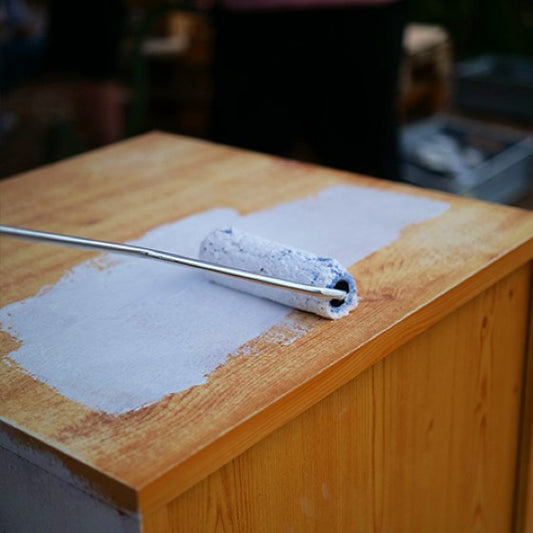 Haftgrund wird mit einer kleinen Rolle auf einem Nachtschränkchen aufgetragen