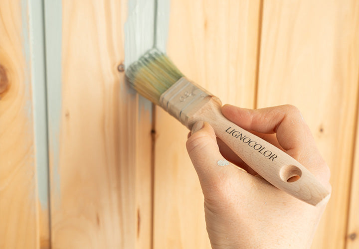 Kreidefarbe wird mit Pinsel auf einer Holzwand aufgetragen