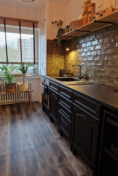 Blick in eine schwarz gestrichene Küche mit dunklen Fliesen und dunklem Holzboden