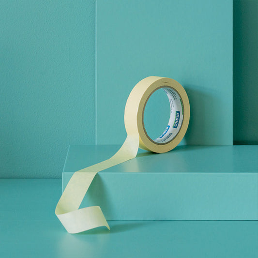 Gelbes Maler-Kreppband leicht abgerollt auf grünem Podest vor grüner Wand