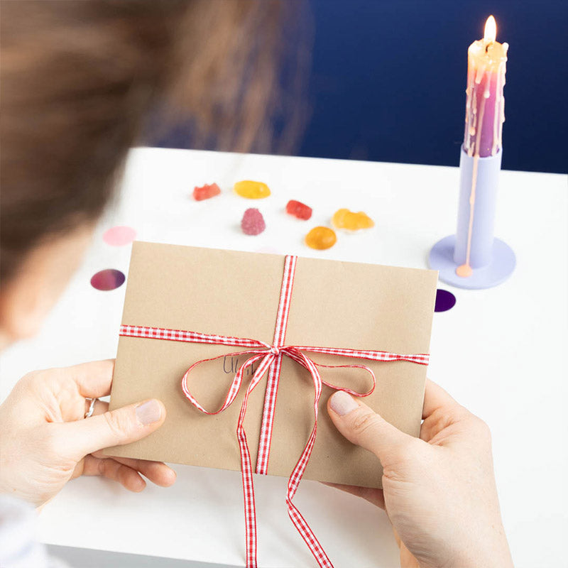 Brauner Umschlag mit rot-weiß karierter Schleife wird in Händen gehalten