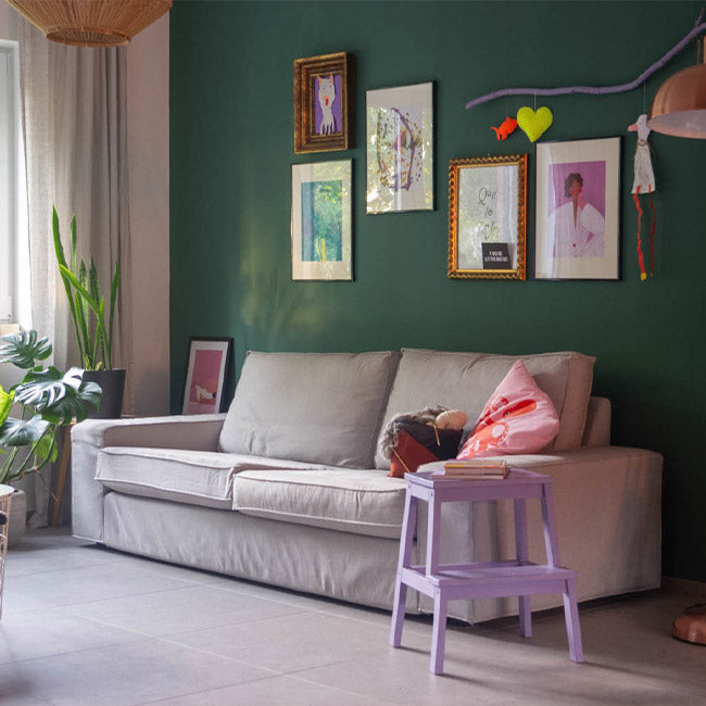 Dunkelgrüne Wand mit Wandbildern vor einem grauen Sofa